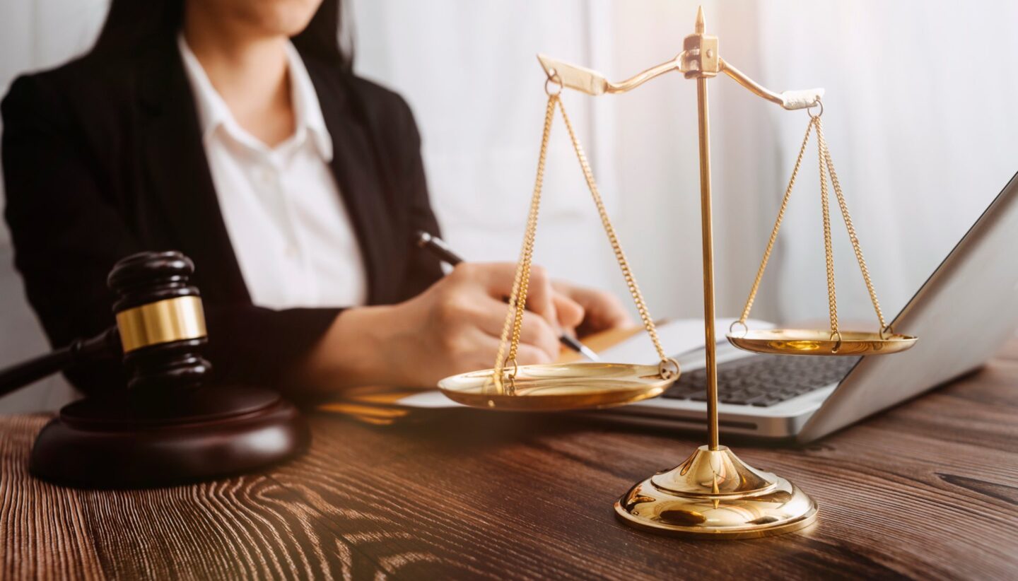 Woman sitting at desk on laptop holding a pen next to a gavel