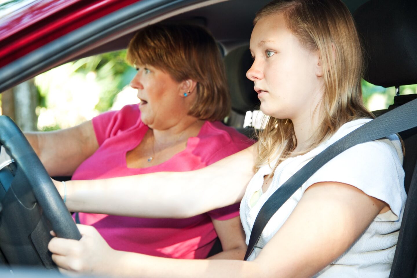 A teen driver with a passenger in a pink shirt that looks scared
