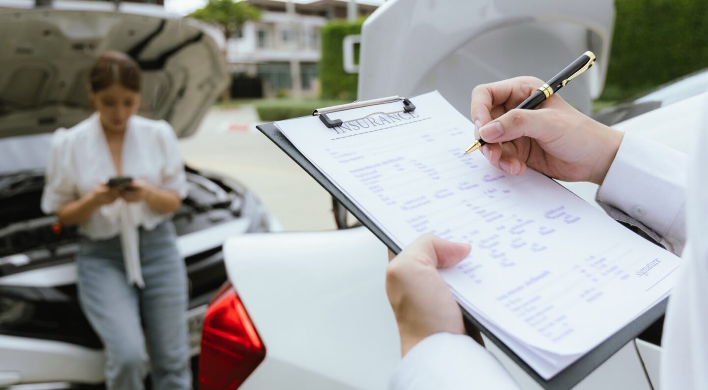 A person on their phone leaning against a white car with the hood up