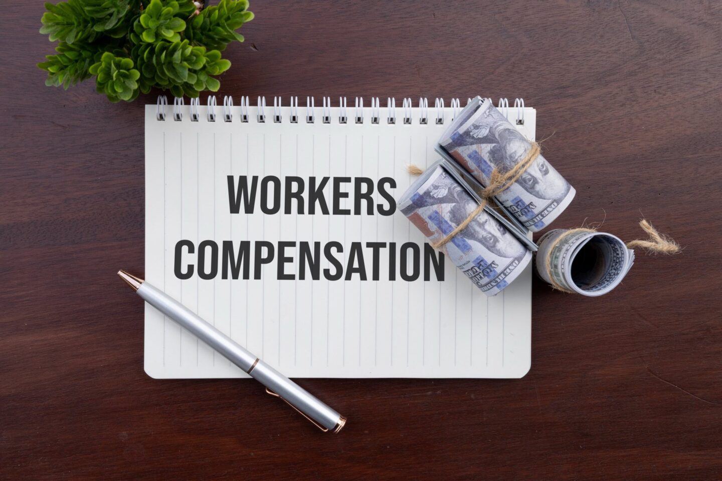 A notebook that says workers compensation with a pen and money