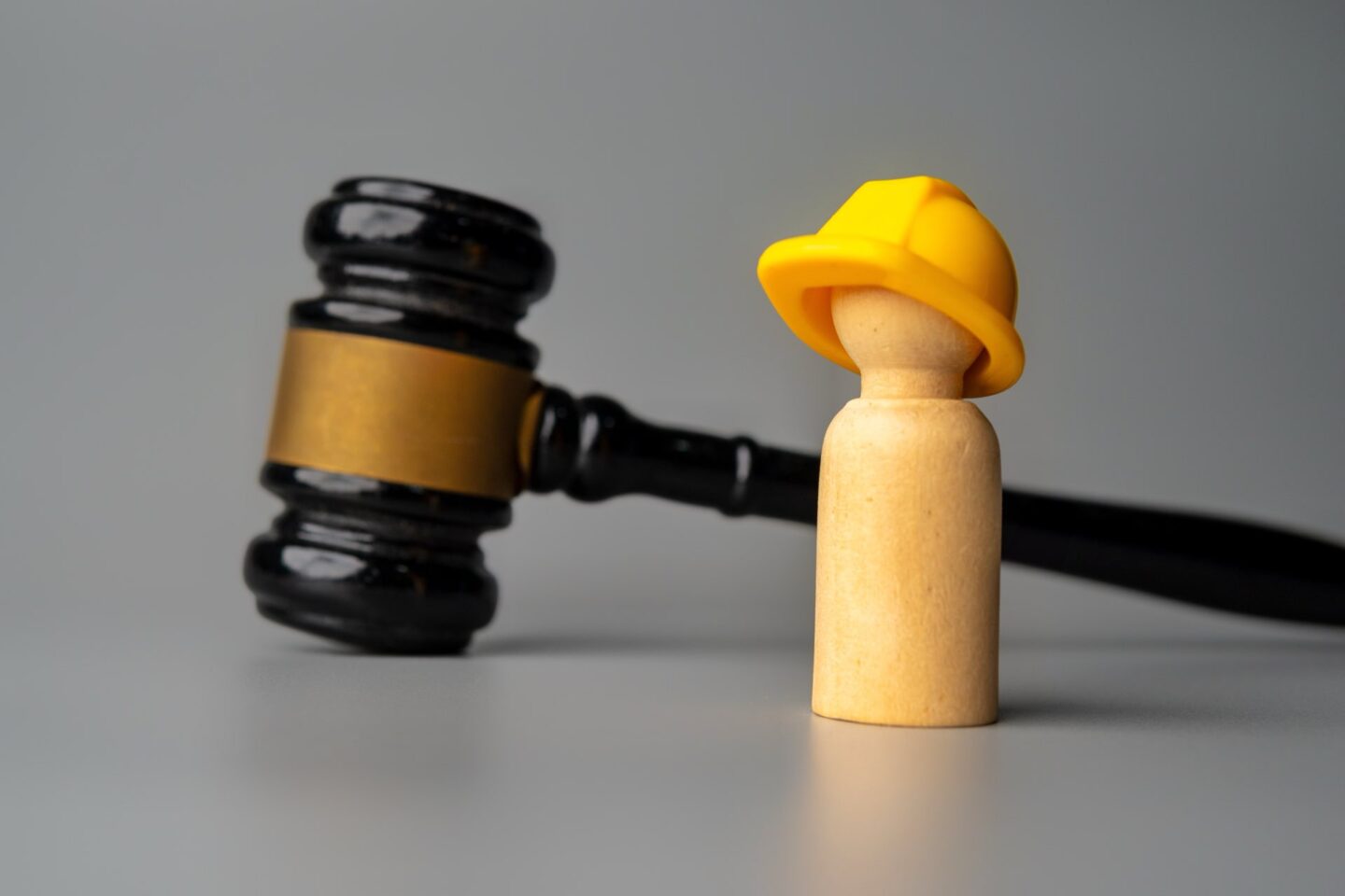 A wooden doll wearing a hard hat stands in front of a gavel.