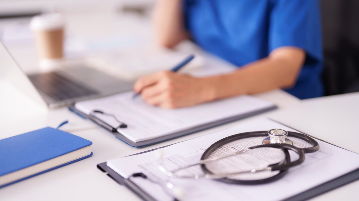 Person sitting at a desk holding a pen in front of a clipboard of paperwork