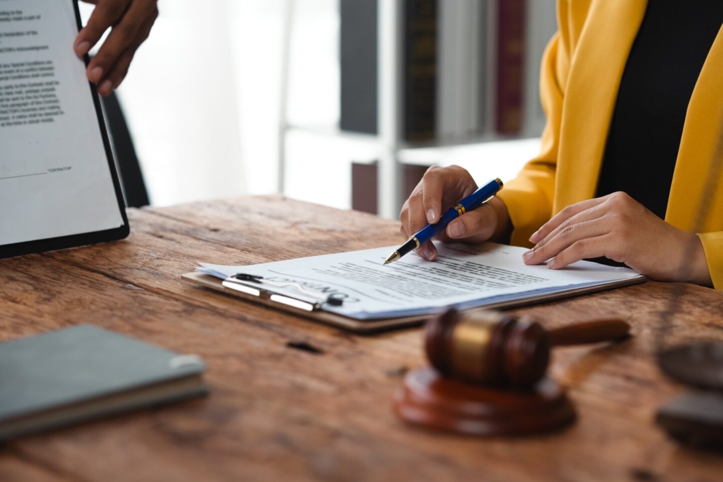 Lawyer showing contract details to client using pen, with gavel and legal documents on wooden desk