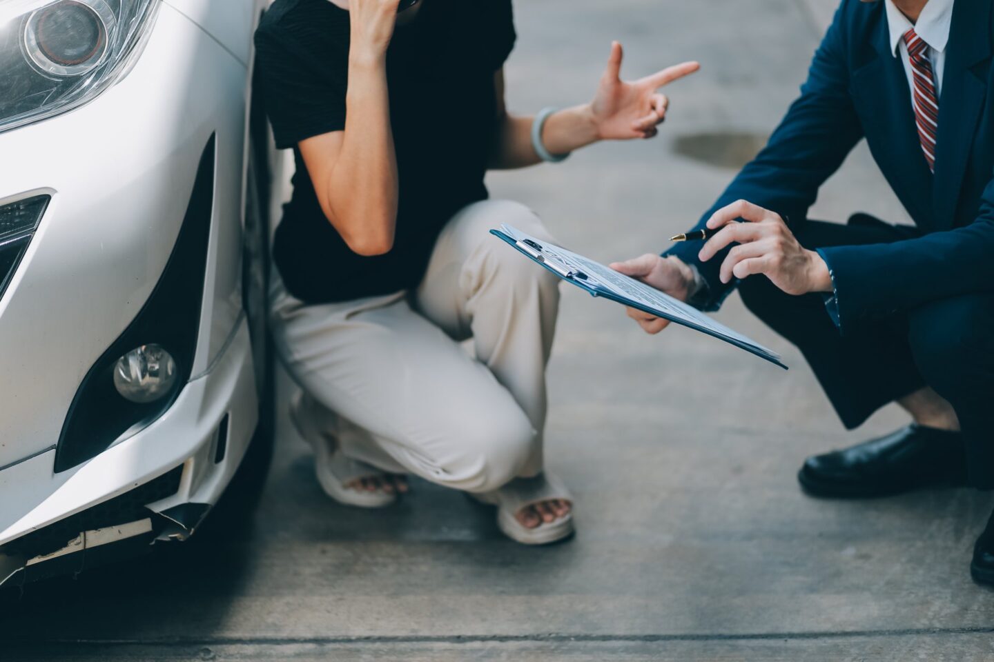 Zoomed in picture of a person in a suit holding a clipboard talking to a lady next to a vehicle