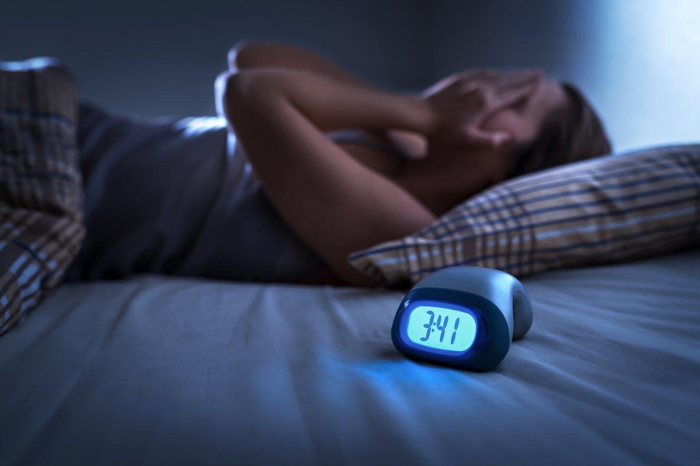 A woman holds her hands over her face in bed, frustrated, next to a digital clock showing 3:41am.