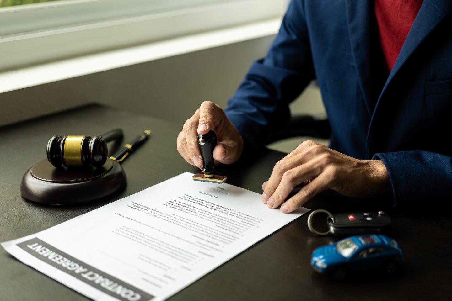 Toy car next to keys and a gavel with someone filling out paperwork
