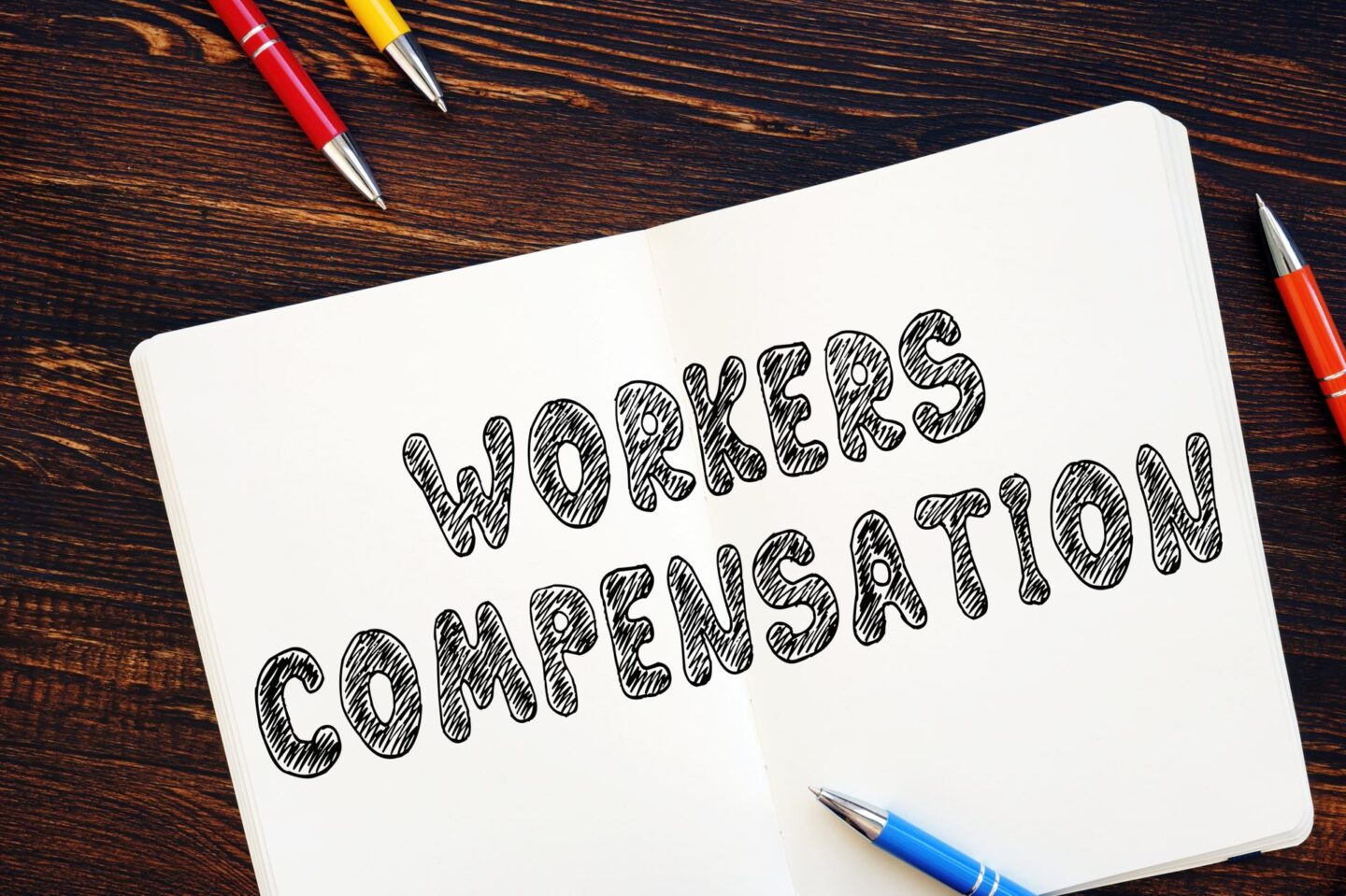 Workers Compensation on white sheet of paper surrounded by four pens
